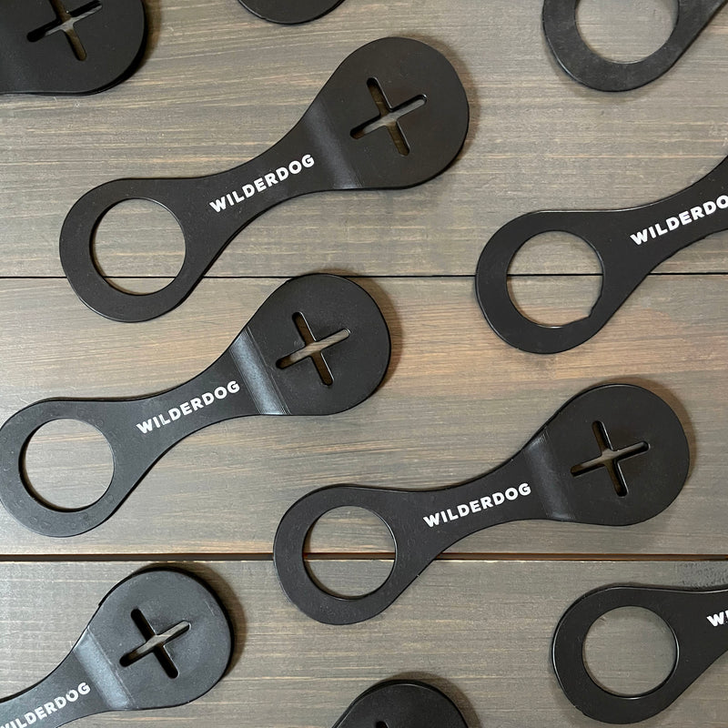 Black Wilderdog bottle openers, each with a circular hole, cross-shaped cutout, and printed logo.